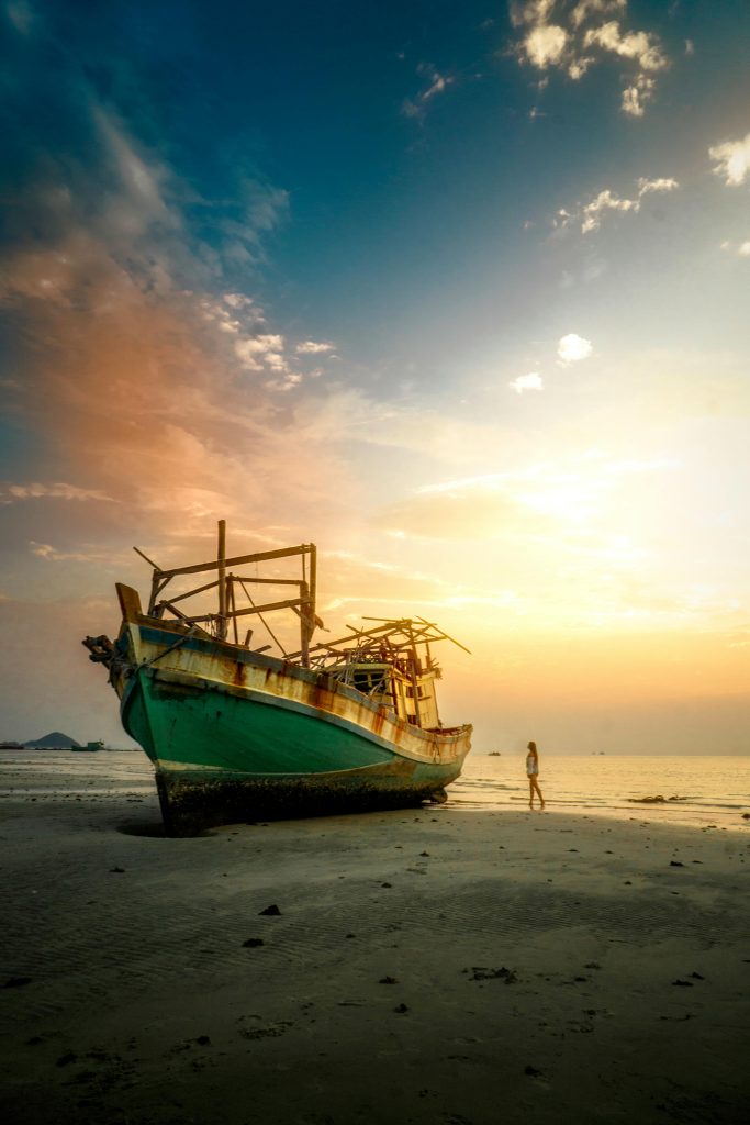 Stunning view of an abandoned fishing boat at sunset on a Thai beach, capturing tranquil beauty and wanderlust.